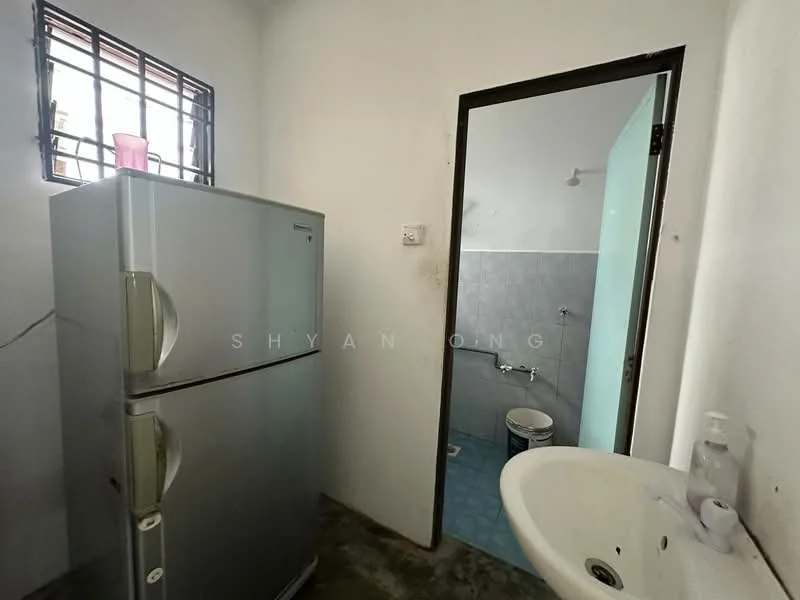 Room features: silver fridge, white sink, blue tiled wall, grey concrete flooring, window with metal grille, light fixture on ceiling, toilet visible in background.