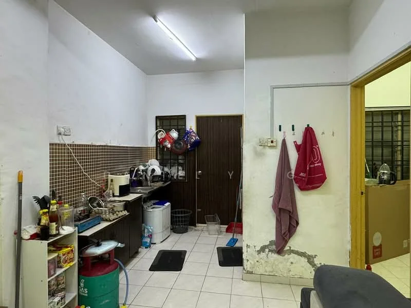 Room features: white painted walls, tile flooring, fluorescent ceiling lights, kitchen countertop, kitchen cabinets, sink, kitchen appliances, black rubber mats, hanging towels, door with security grill, broom and cleaning supplies, water container.