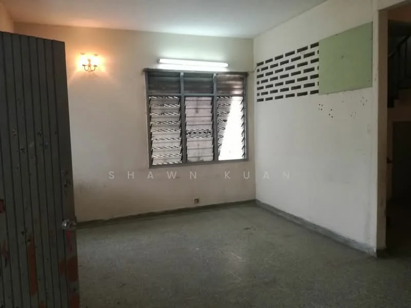 Room features: grey terrazzo flooring, white painted walls, window with metal grilles, wall-mounted light fixture, fluorescent ceiling light, exposed brick wall section, corner with staircase visible.