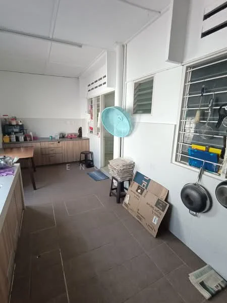 Kitchen features: white painted walls, grey tiled flooring, wood cabinetry, countertop with space for appliances, window with metal grille, wall-mounted fan, hanging pots, open shelving, sink, stool, stack of cardboard boxes.