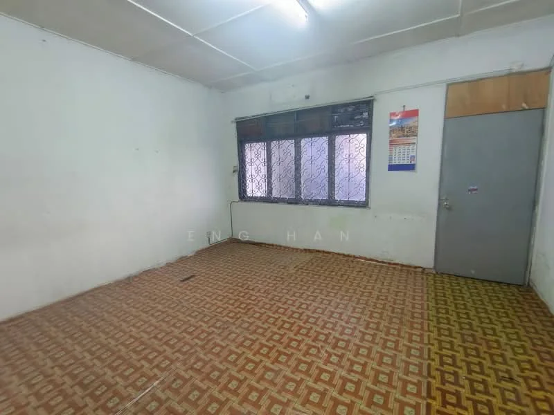 Room features: white painted walls, vinyl flooring with geometric pattern, window with metal grille, door with metal frame, ceiling with fluorescent lighting, calendar on wall, empty space, no visible furniture.
