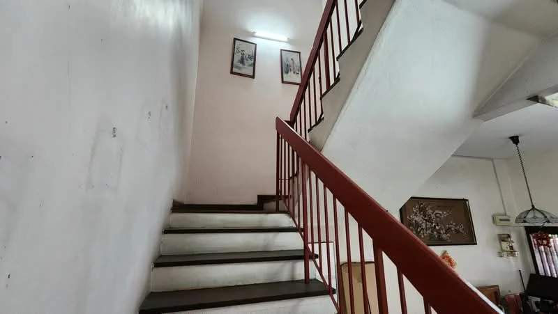 Room features: white painted walls, wooden staircase with red railing, framed artwork on walls, ceiling light fixture.