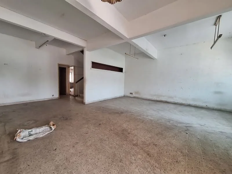 Room features: bare concrete flooring, white painted walls, exposed ceiling beams, large open space, no visible fixtures or furniture, natural light from windows, staircase visible in background, unfinished appearance; style: minimalist.