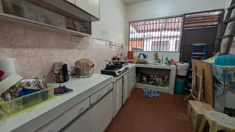 Kitchen features: white cabinetry, pink tiled backsplash, laminate countertop, single-bowl stainless-steel sink, chrome pull-down faucet, freestanding gas stove, exposed brick wall, ceramic tile flooring, window with security bars, various kitchen utensils and appliances, plastic storage containers, cleaning supplies, stacked chairs, laundry basket.