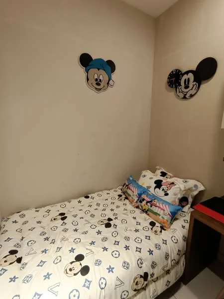 Bedroom features: single bed with Mickey Mouse bedding, decorative pillows with Mickey Mouse design, light-colored painted walls, Mickey Mouse wall art, wooden bedside table, laminate flooring; style: children's.