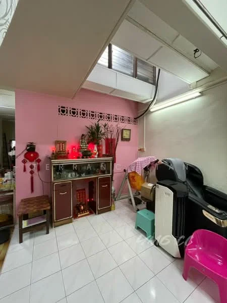 Room features: pink painted walls, white tiled flooring, exposed ceiling with beams, decorative wall paneling, small wooden table, black cabinet, decorative items on cabinet, clothes drying rack, air conditioning unit, red lanterns, small seating area; style: modern.