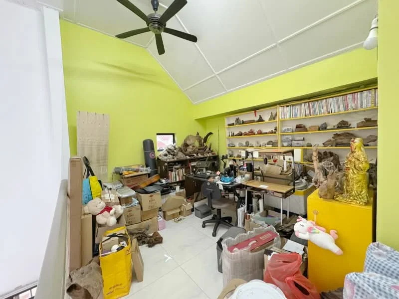 Room features: lime green painted walls, white ceiling with exposed beams, ceiling fan, tile flooring, wooden shelving with books, cluttered workspace with sewing machine, various boxes and storage items, decorative figurines, office chair, yellow storage unit, multiple decorative items.