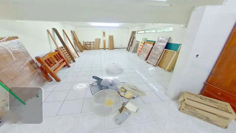 Room features: white painted walls, glossy white tile flooring, ceiling fan, wooden furniture, stacked wooden panels, cardboard boxes, green wall section, large windows, unfurnished space.