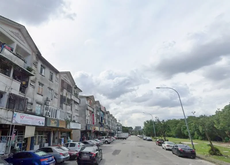 Exterior type: shophouse; features: multi-storey shophouses, balconies with railings, ground floor retail spaces, signage on storefronts, street parking, tree-lined street, cloudy sky, urban setting; style: traditional.