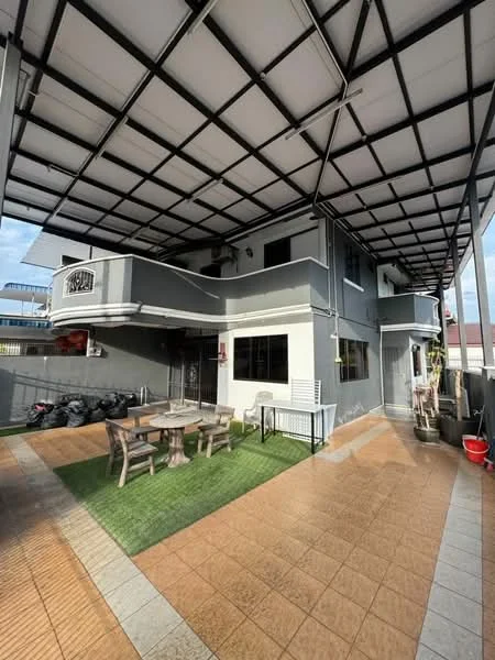 Exterior type: semi-detached house; features: grey painted facade, flat roof with exposed beams, outdoor patio area, manicured lawn, wooden dining table with chairs, paved flooring, fenced perimeter, outdoor seating area, garden area, multiple levels, parking space visible; style: modern.