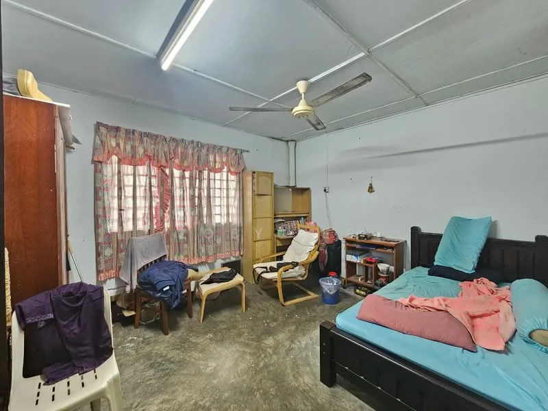 Bedroom features: king-size bed with blue bedding, wooden bed frame, 2 wooden chairs, wooden wardrobe, bookshelf, ceiling fan, curtains with floral pattern, concrete flooring, desk with items, laundry basket.