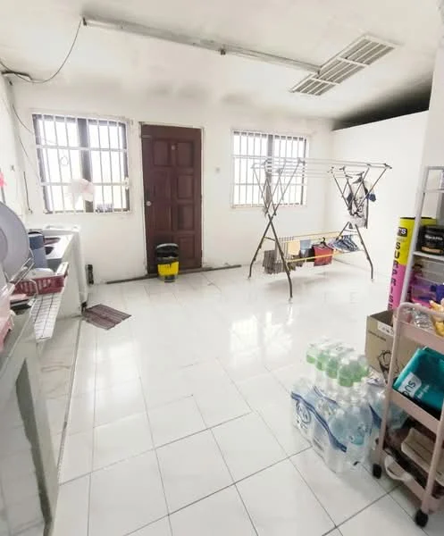 Laundry features: white tiled flooring, white painted walls, two windows with metal grilles, wooden door, clothes drying rack, washing machine, plastic storage shelves, broom and mop holder, water bottles, bucket, utility sink.
