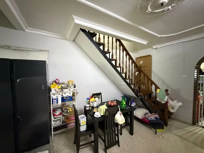 Room features: grey painted walls, exposed concrete flooring, wooden staircase, white ceiling with decorative rose, recessed lighting, black refrigerator, metal shelving unit with various items, wooden dining table, plastic chairs, various bags and items on the floor; style: traditional.