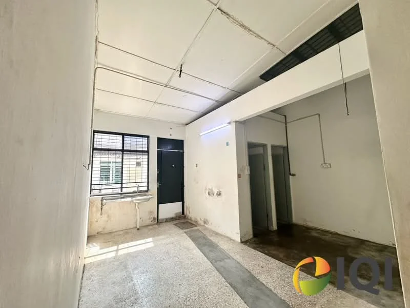 Room features: white painted walls, exposed ceiling with visible beams, concrete flooring, large window with metal grille, doorway leading to another room, light fixture on ceiling, wall-mounted electrical outlets, no visible furniture or decor; style: minimalist.