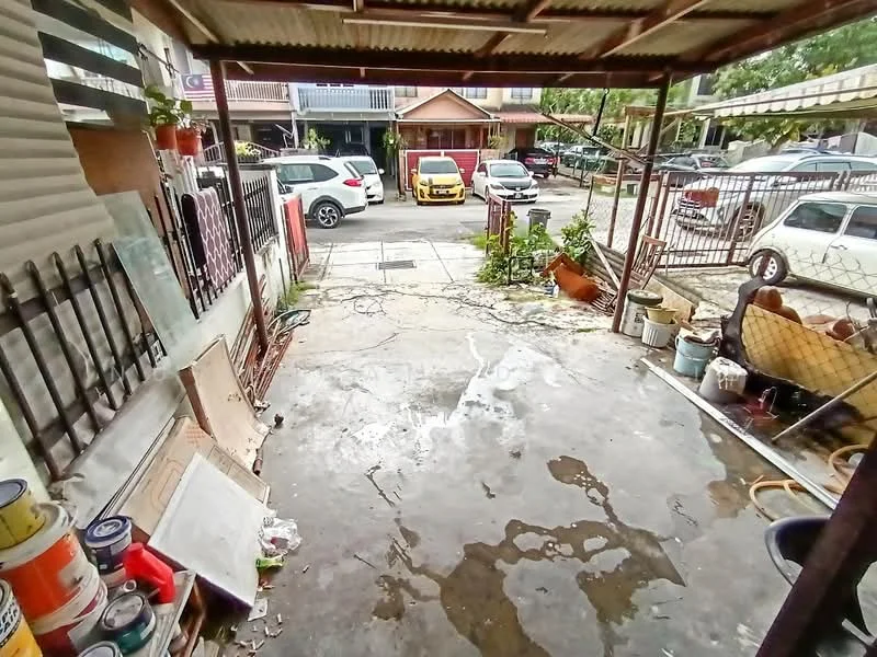 Exterior type: car porch; features: concrete flooring, metal roof, fenced area, potted plants, visible vehicles on street, drainage channel, outdoor storage items, open space, surrounding residential buildings.