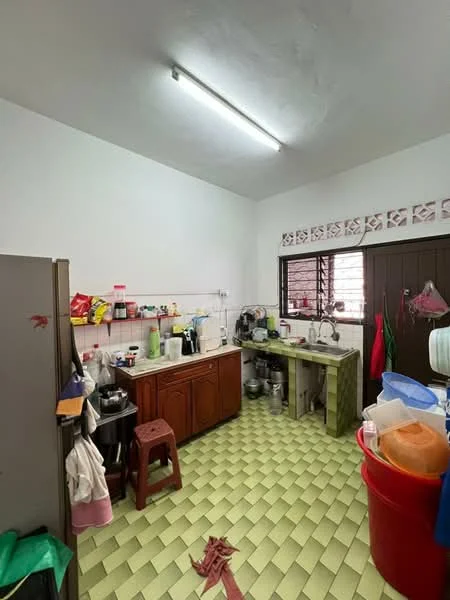 Kitchen features: green and yellow checkered tile flooring, white painted walls, fluorescent ceiling light, wooden cabinetry, stainless-steel sink, chrome faucet, built-in countertop, kitchen appliances visible, stool, various kitchen utensils and containers.