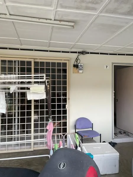 Room features: grilled security door, light-colored painted walls, concrete flooring, ceiling with grid panels, clothes drying rack, plastic storage boxes, single chair, electrical meter box.