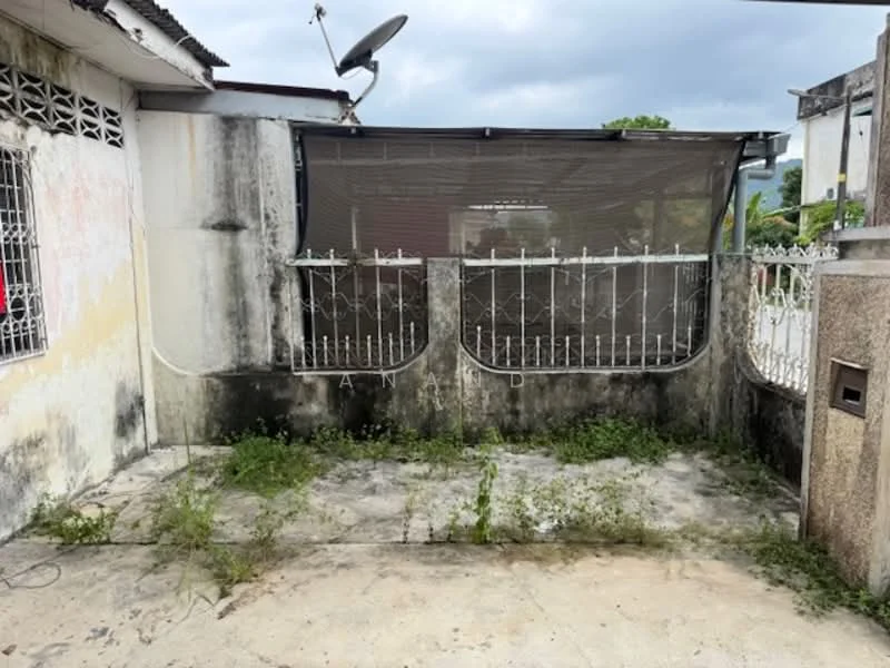 Exterior features: concrete flooring, overgrown grass, metal gate, fence with decorative design, satellite dish, partially covered area, weathered walls, exposed concrete, surrounding greenery.