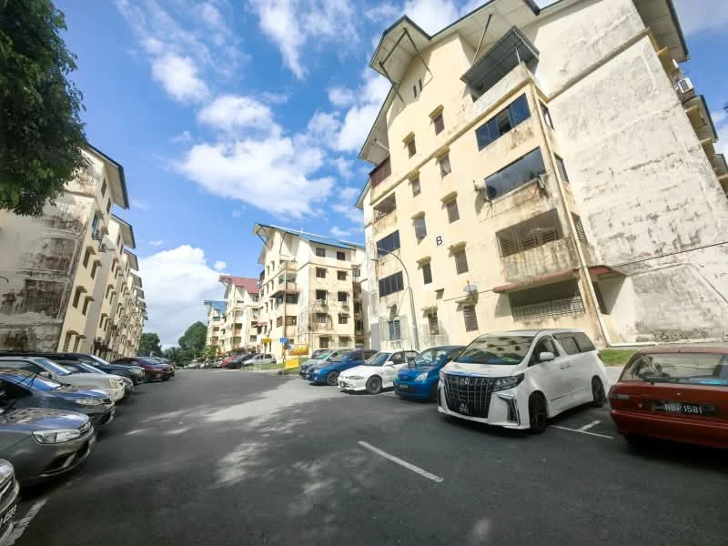 Exterior type: low-rise apartment block; features: multiple storey buildings, exposed concrete facade, balconies on upper floors, parking lot with multiple vehicles, manicured landscaping, clear blue sky, surrounded by greenery; style: modern.