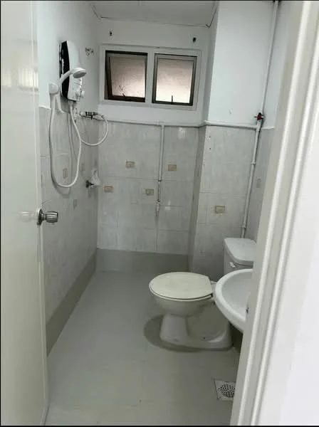 Bathroom features: white tiled walls, light grey floor tiles, toilet, sink, shower with wall-mounted showerhead, mirror above sink, window for natural light, shower curtain rod, wall-mounted water heater.