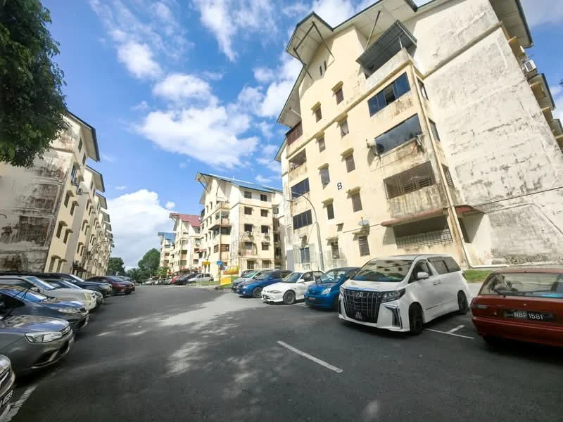 Exterior type: low-rise apartment block; features: multiple-storey buildings, exposed concrete facade, balconies with metal railings, parking lot with multiple vehicles, landscaped trees, clear blue sky, surrounding greenery; style: traditional.