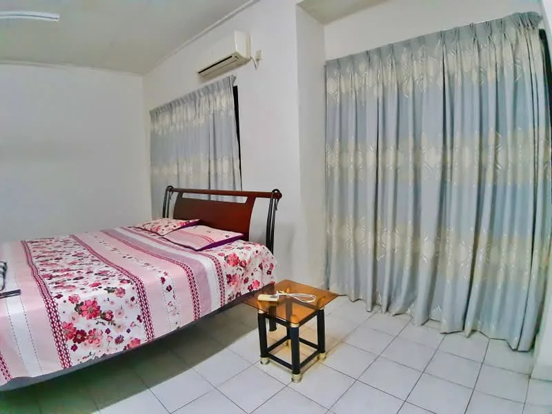 Bedroom features: queen-size bed with floral bedding, 2 bedside tables, curtains with floral pattern, wall-mounted air conditioning unit, white painted walls, tiled flooring, decorative wall art, light fixture on ceiling.