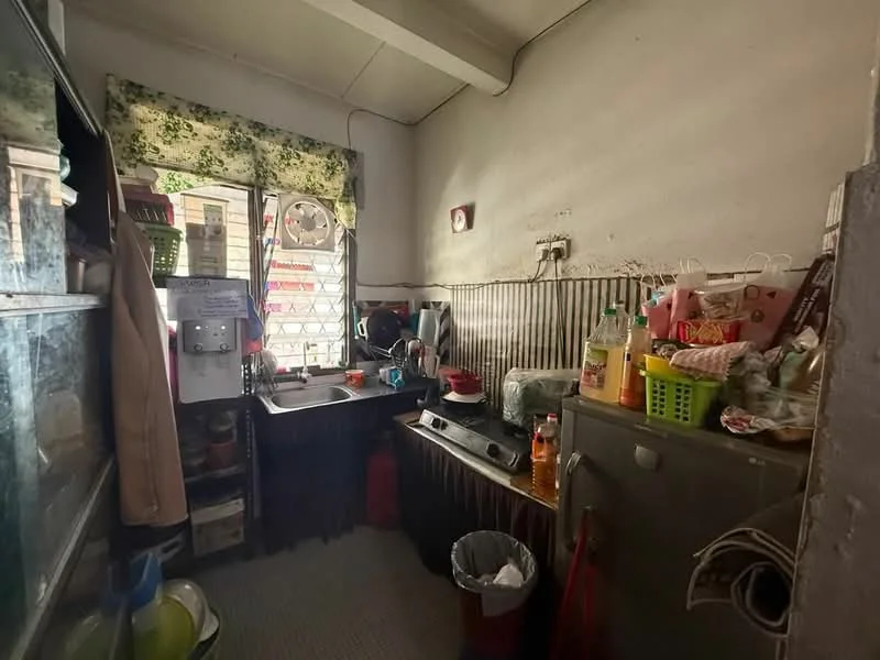 Kitchen features: single-bowl stainless-steel sink, chrome pull-down faucet, wood cabinetry, countertop with clutter, refrigerator, stove, kitchen utensils, window with floral curtain, tile flooring, garbage bin, plastic storage baskets.