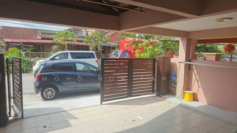 Exterior type: linked terrace house; features: sliding gate, paved driveway, manicured landscaping, front yard, car parked in driveway, surrounding residential area, visible street view, red house in background, green plants, water hose, yellow bucket; style: modern.