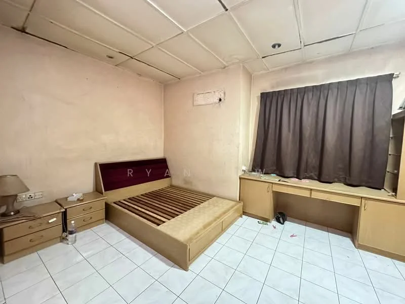 Bedroom features: single bed frame without mattress, two wooden bedside tables, desk with drawers, brown curtain, white tiled flooring, plain beige walls, ceiling with visible tiles, light fixture on ceiling.