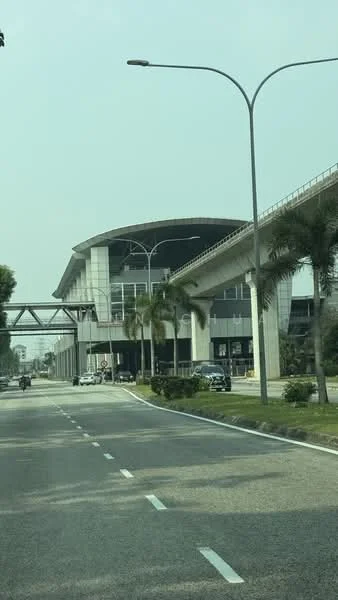 Exterior type: commercial building; features: glass curtain wall, flat roof, elevated monorail track, palm trees in landscaping, manicured green spaces, multiple vehicle lanes, modern architectural design, large overhang, visible parking area; style: modern.