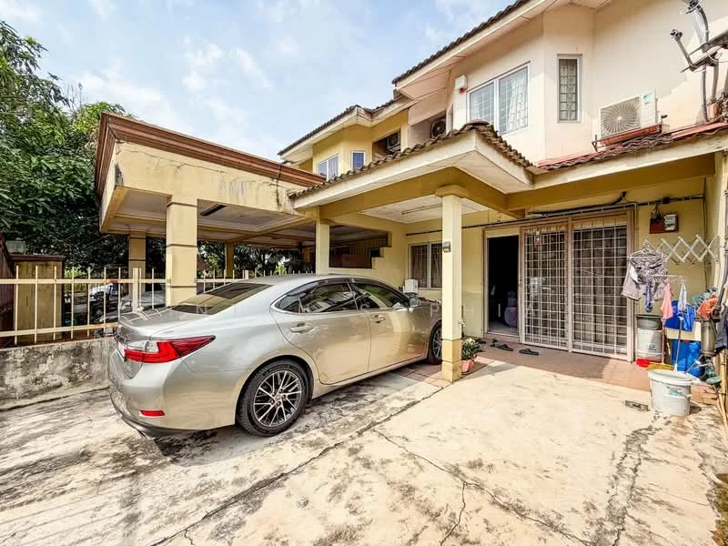 Exterior type: semi-detached house; features: car porch with awning, driveway with concrete surface, two-storey structure, exposed brick facade, sloping tiled roof, front garden area with plants, security grille on entrance, air conditioning unit visible, windows with metal grilles, parking space for one vehicle; style: modern.