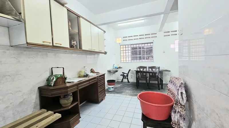 Kitchen features: white tiled walls, light blue tiled flooring, wood cabinetry with gold handles, open shelving, countertop with space for appliances, sink, window with grid pattern, stool, bucket, work table, wooden bench.