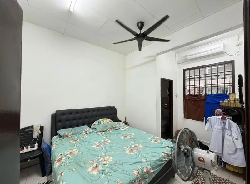 Bedroom features: queen-size bed with upholstered headboard, floral patterned bedding, ceiling fan, wall-mounted air conditioning unit, window with security bars, white painted walls, tile flooring, decorative rug, clothes hanging on a rack, chair in the corner.