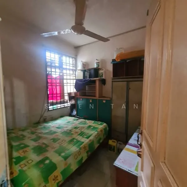 Bedroom features: single bed with green patterned bedding, wooden wardrobe, wooden shelving unit, ceiling fan, window with metal grille, light-colored walls, tile flooring, small desk, colorful curtains.