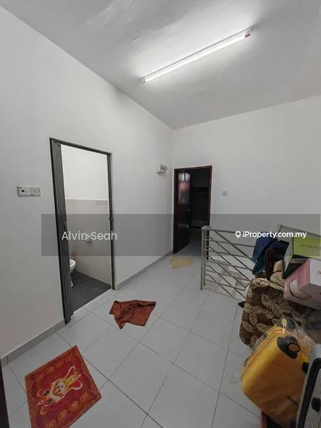 Room features: white painted walls, sloped ceiling, fluorescent ceiling light, white tiled flooring, metal railing, doorway leading to bathroom, window with no visible treatment, decorative rug, cluttered with personal items.
