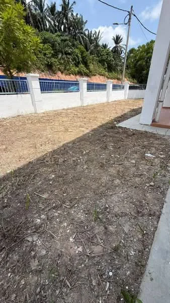 Exterior features: bare ground, fenced perimeter, white painted wall, surrounding greenery, paved pathway, utility poles visible, open space.