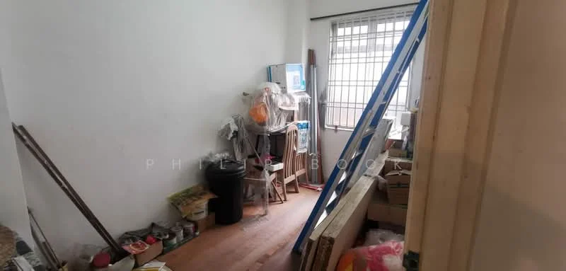 Room features: white painted walls, wooden flooring, window with security bars, storage boxes, cleaning supplies, ladder, trash bin, broom, mop, various household items.
