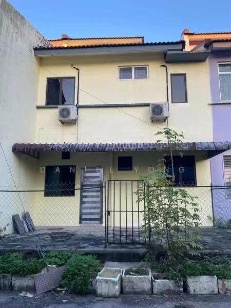Exterior type: linked terrace house; features: yellow painted facade, two-storey building, two wall-mounted split AC units, gated entrance, fenced front yard, slate stone pathway, overhanging roof with tiles, windows with grills, front door with wooden frame, mature shrubbery in front yard; style: modern.