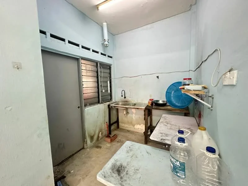 Room features: light blue painted walls, concrete flooring, single-bowl stainless-steel sink, wall-mounted faucet, wooden table, plastic water container, metal bowl, shelves, window with metal grilles, door with handle.