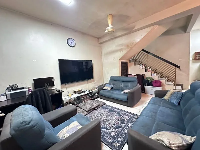 Living features: 2-seater fabric sofa in blue, 3-seater fabric sofa in blue, area rug with intricate pattern, wall-mounted TV, TV console, ceiling fan, clock on wall, exposed concrete walls, tile flooring, staircase in background, decorative items on shelves.