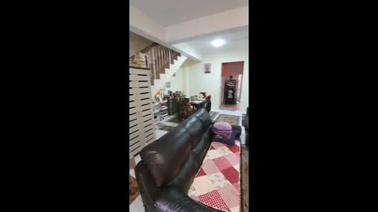 Living features: black leather sofa, area rug with patchwork design, wooden staircase, white painted walls, recessed ceiling lights, wooden storage cabinet, small round table, decorative wall art, flooring with tiles, open layout to adjacent room; style: modern.