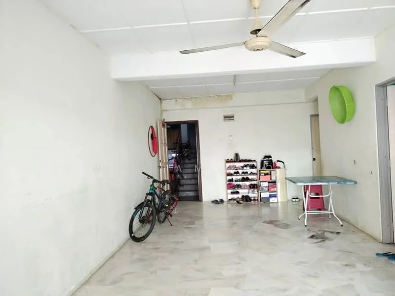 Room features: white painted walls, marble flooring, ceiling fan, staircase visible in background, bicycle, shoe rack, ironing board, green wall decoration.