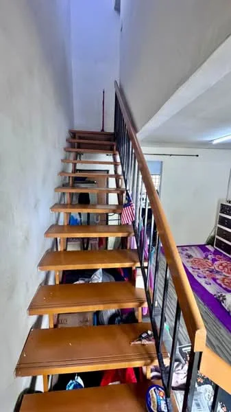 Room features: wooden staircase, metal railing, white painted walls, carpeted landing, cluttered space, visible bedding, storage boxes, decorative items.