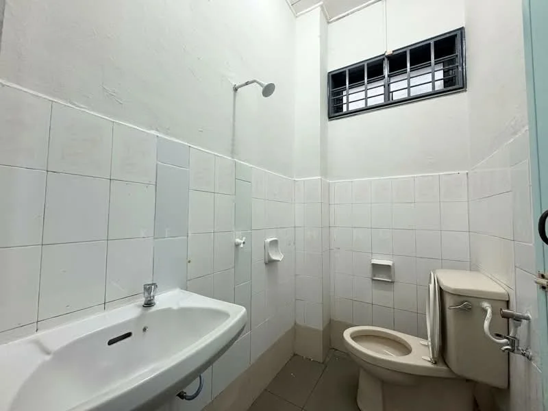 Bathroom features: white tiled walls, grey tiled flooring, single-bowl sink, chrome faucet, toilet, shower head, window with metal grille, toilet paper holder, soap holder.