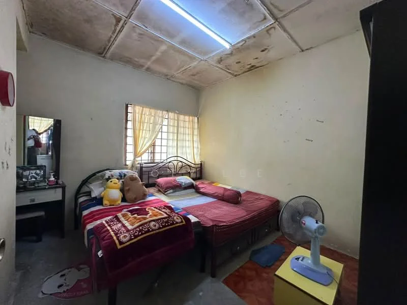 Bedroom features: two single beds with bedding, wooden bed frame, decorative throw blanket, stuffed toys on bed, mirror on dresser, window with sheer curtains, ceiling fan, light fixture on ceiling, wooden flooring, wall with visible marks and stains.