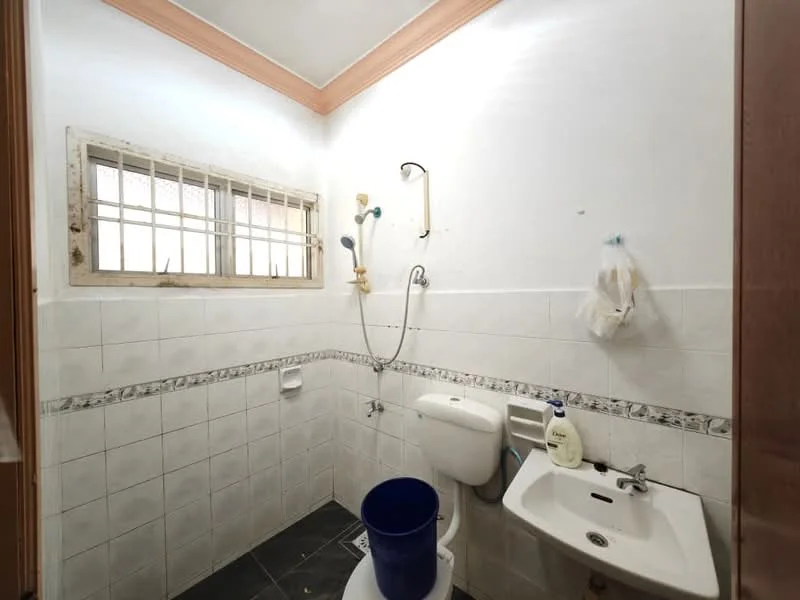 Bathroom features: white tiled walls, grey tiled flooring, shower with handheld showerhead, toilet, sink with wall-mounted faucet, window with metal bars, decorative border tile, bucket.