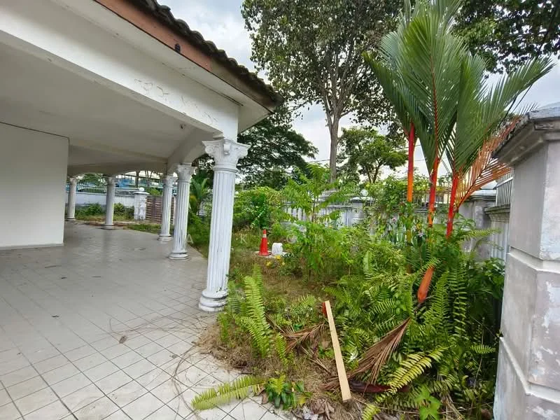 Exterior features: covered porch area, columns with decorative capitals, tiled flooring, overgrown landscaping, tropical plants, fence, garden area, trees, paved walkway.
