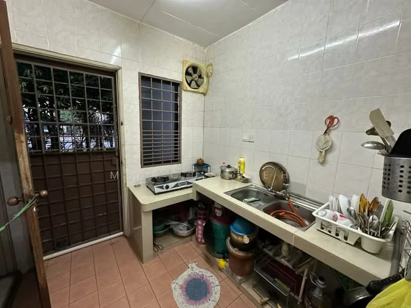 Kitchen features: white tiled walls, pink ceramic tile flooring, single-bowl stainless-steel sink, chrome pull-down faucet, gas stove with two burners, kitchen countertop, wooden door, window with metal grille, exhaust fan, storage cabinets, various kitchen utensils, plastic containers, decorative rug.
