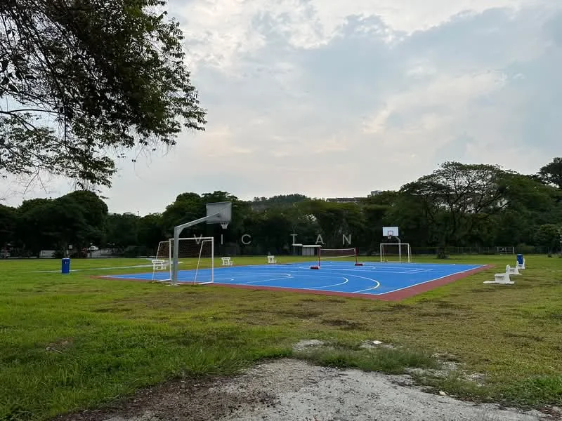 Exterior type: landscape garden; features: outdoor basketball court with blue surface, two basketball hoops, surrounding grassy area, mature trees in background, park benches, open space, cloudy sky; style: modern.