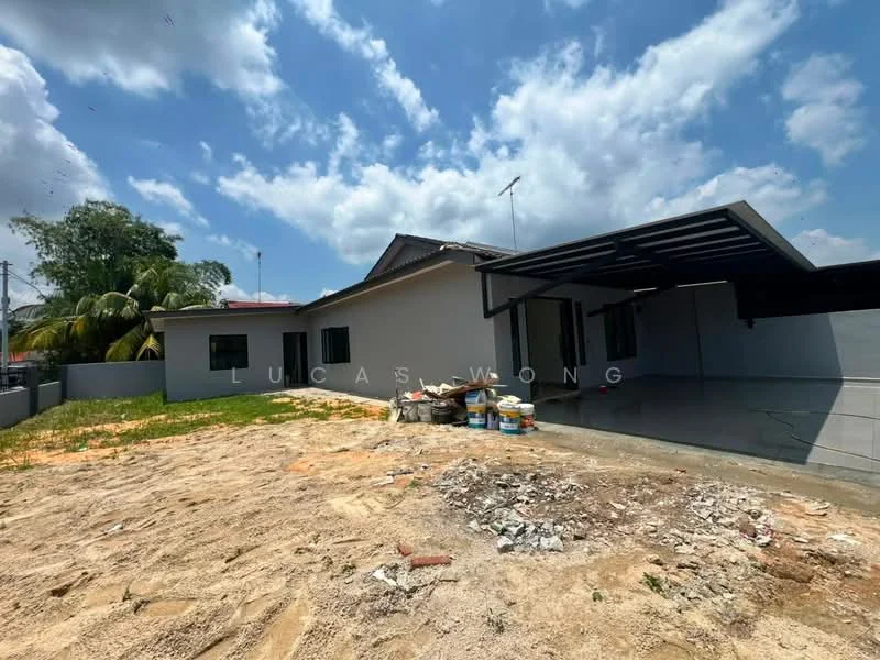 Exterior type: detached bungalow; features: flat roof, cream painted facade, covered car porch, manicured lawn, paved driveway, surrounded by greenery, outdoor space with construction materials; style: modern.